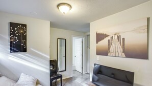 Quarto de hotel com cama, área de estar com televisão, pintura de um cais e porta que dá para outro quarto.