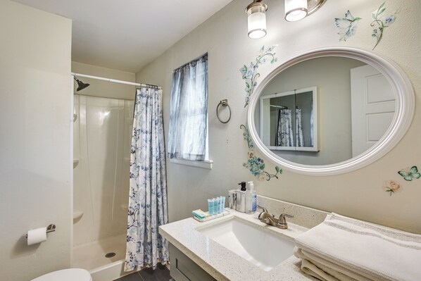 A bathroom with a shower, toilet, sink, and a mirror.