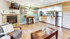 Un salon avec une cheminée, un téléviseur fixé au-dessus et une table basse en bois.