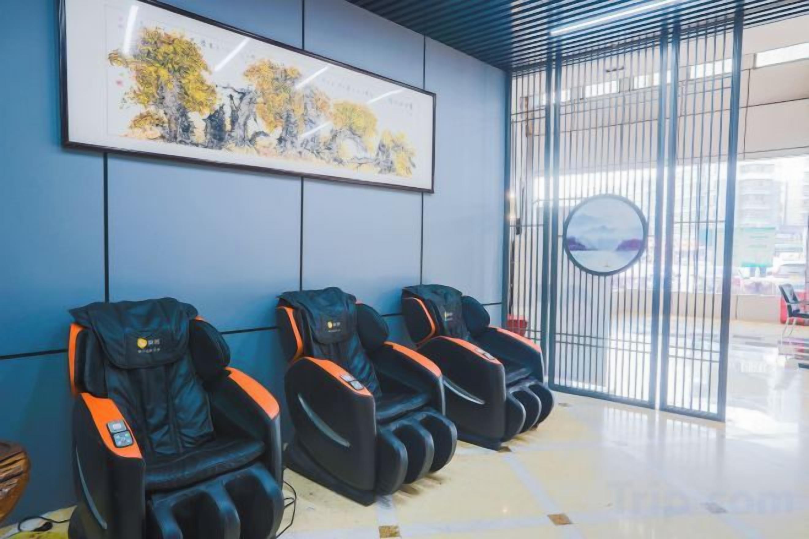 A waiting area with massage chairs, a framed artwork, and a view through a window.