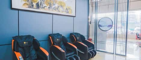 A waiting area with massage chairs, a framed artwork, and a view through a window.