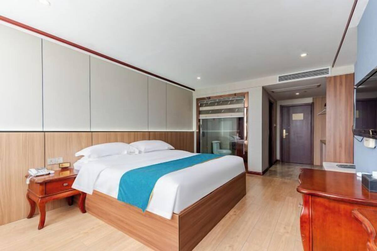 A hotel room with a large bed, wooden headboard, a bedside table with a phone, and a wardrobe with sliding doors.