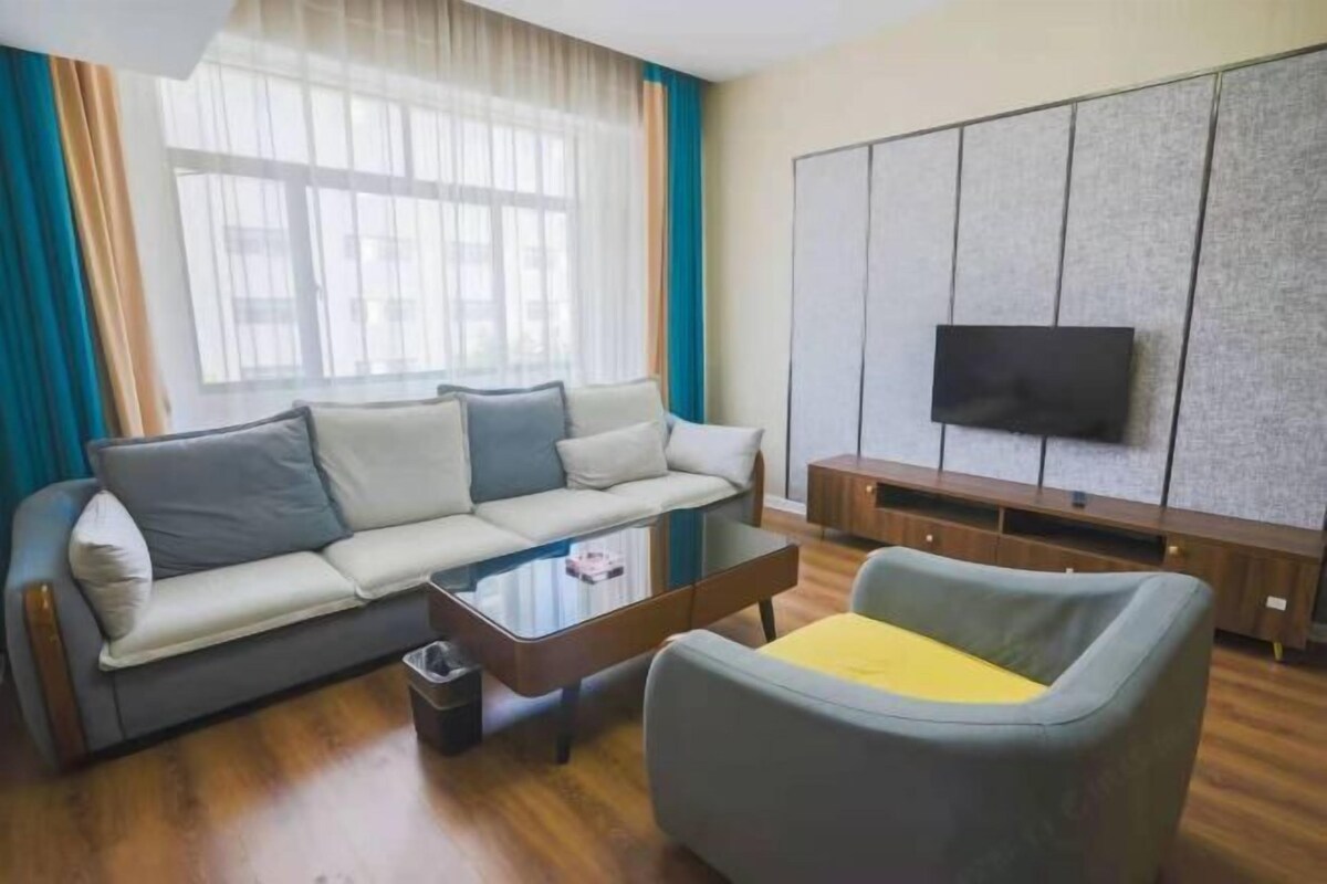 A modern living room with a sofa, armchair, coffee table, and a TV mounted on a textured wall.