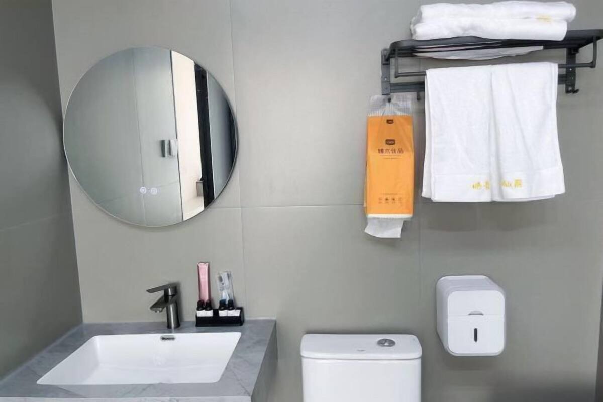A modern bathroom with a round mirror, a sink, a toilet, and a towel rack with folded towels.