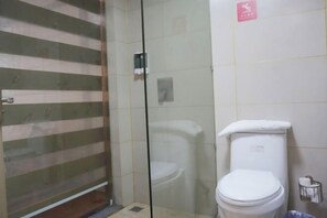 Un baño con cabina de ducha de vidrio, inodoro blanco y un cubo de basura.