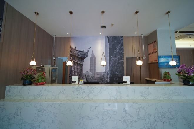 Zona de recepción de hotel con mostrador de mármol, lámparas colgantes y un gran mural con vistas a la ciudad.