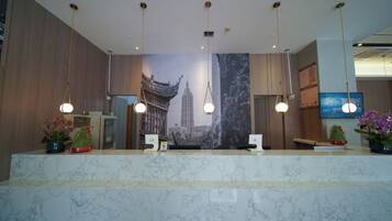 Zona de recepción de hotel con mostrador de mármol, lámparas colgantes y un gran mural con vistas a la ciudad.
