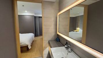 Un baño de hotel moderno con un espejo grande, un lavamanos y una zona de ducha.