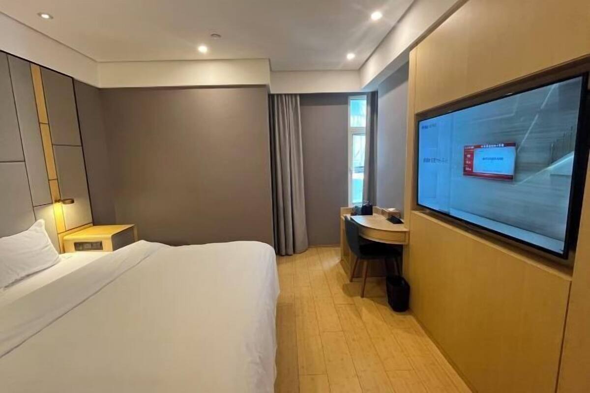 Ein Hotelzimmer mit Bett, Schreibtisch, Fernseher und einem fenster mit Vorhängen.