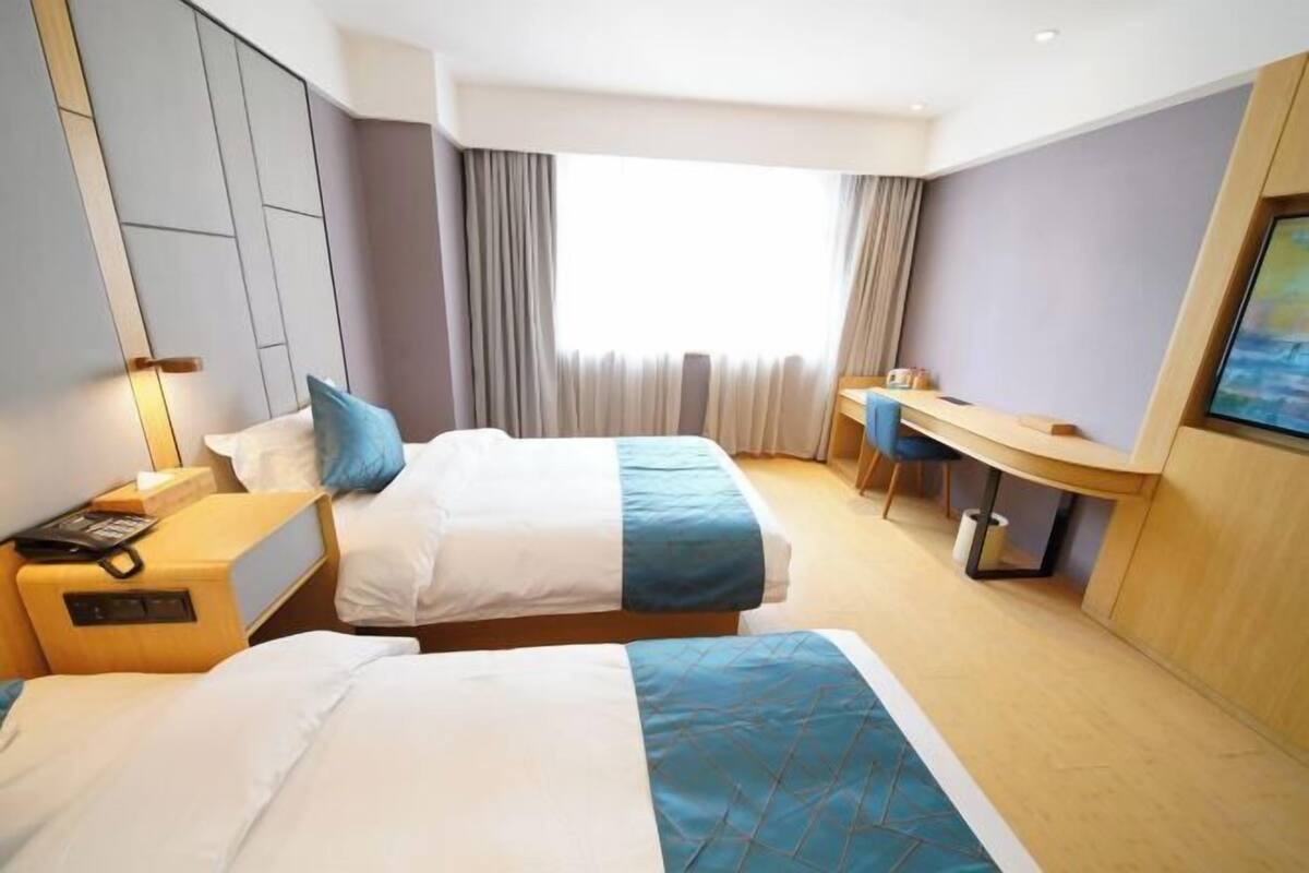 Ein Hotelzimmer mit zwei Betten, einem Schreibtisch, einem Stuhl und einem großen Fenster mit Vorhängen.