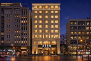 Un hotel amb façana moderna, diverses plantes i finestres il·luminades.