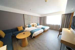 Habitación de hotel con sofá, dos camas, una mesa redonda, un escritorio y televisor.