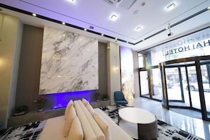 Un vestíbulo de hotel con pared de mármol, mostrador de recepción y zona de estar.