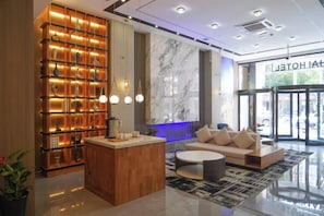 A hotel lobby with a reception desk, a seating area with a sofa and chairs, a wooden bookshelf, and a marble wall. - Shanghai Huaihai Hotel (Shanghai)