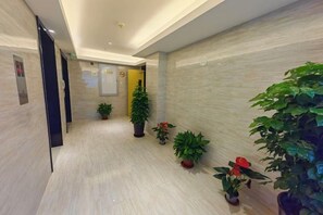 A hallway with a light-colored floor, potted plants, and a door with a sign. - Shanghai Huaihai Hotel (Shanghai)