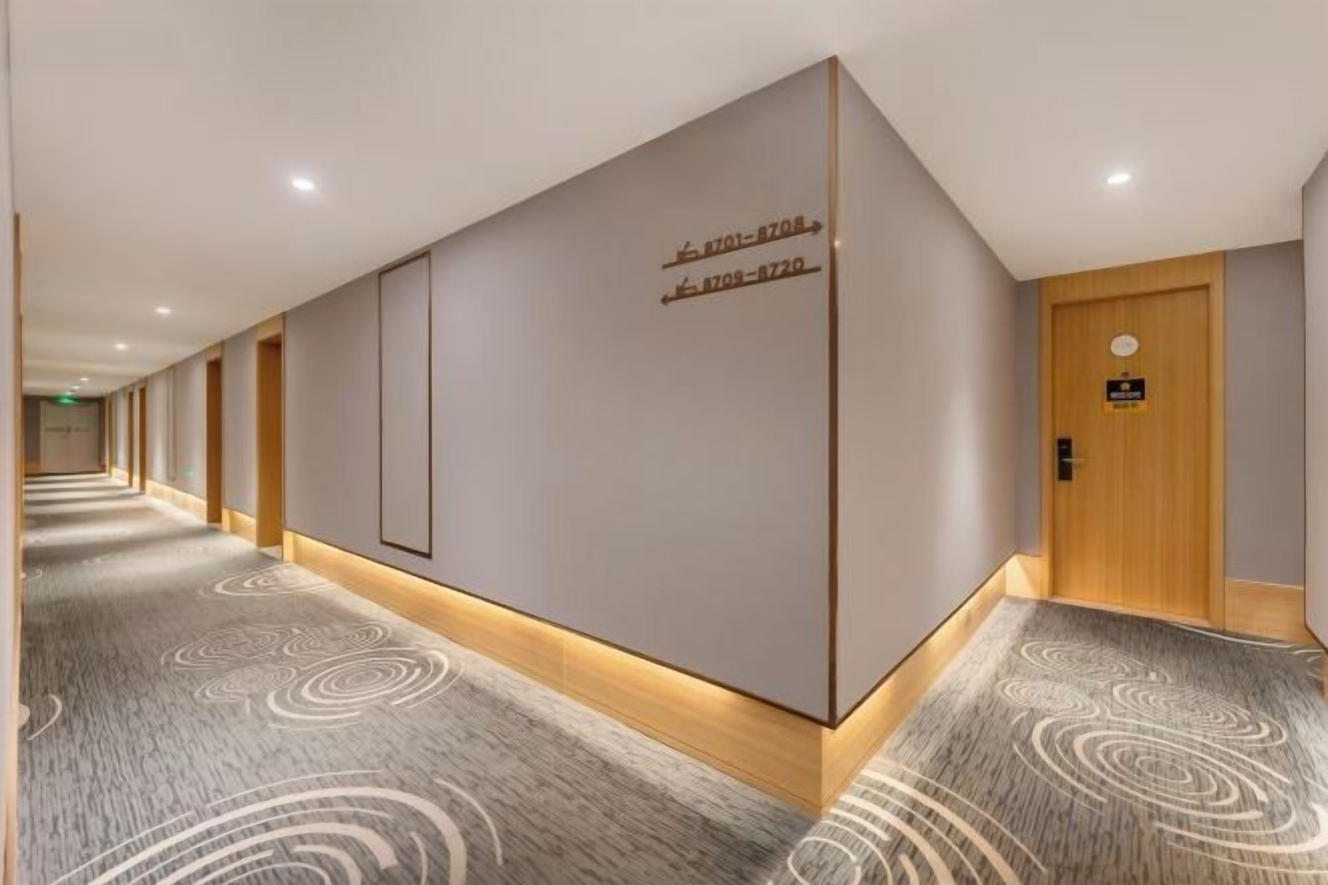 A hotel hallway with directional signs, a wooden door, and patterned carpet.