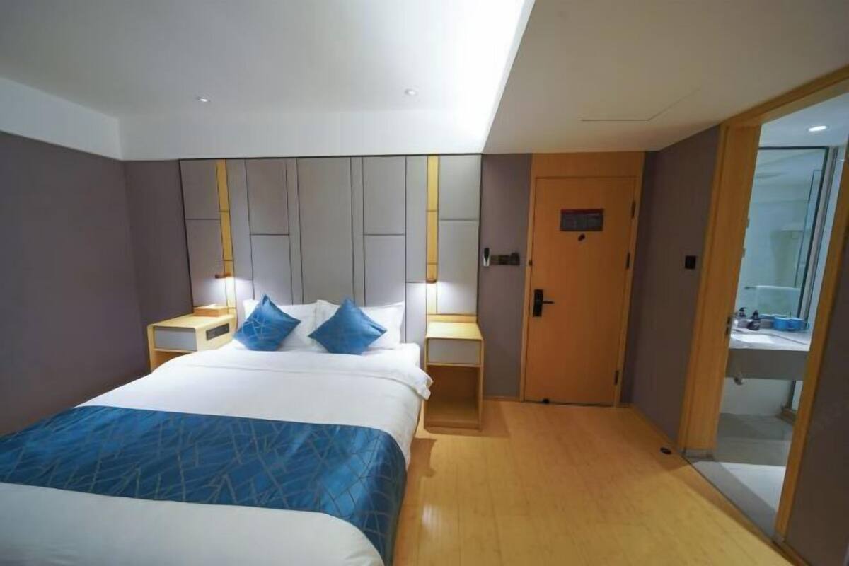 Ein modernes Hotelzimmer mit einem großen Bett, Nachttischen, einem Kleiderschrank und einem durch eine Glastür einsehbarer Badezimmer.