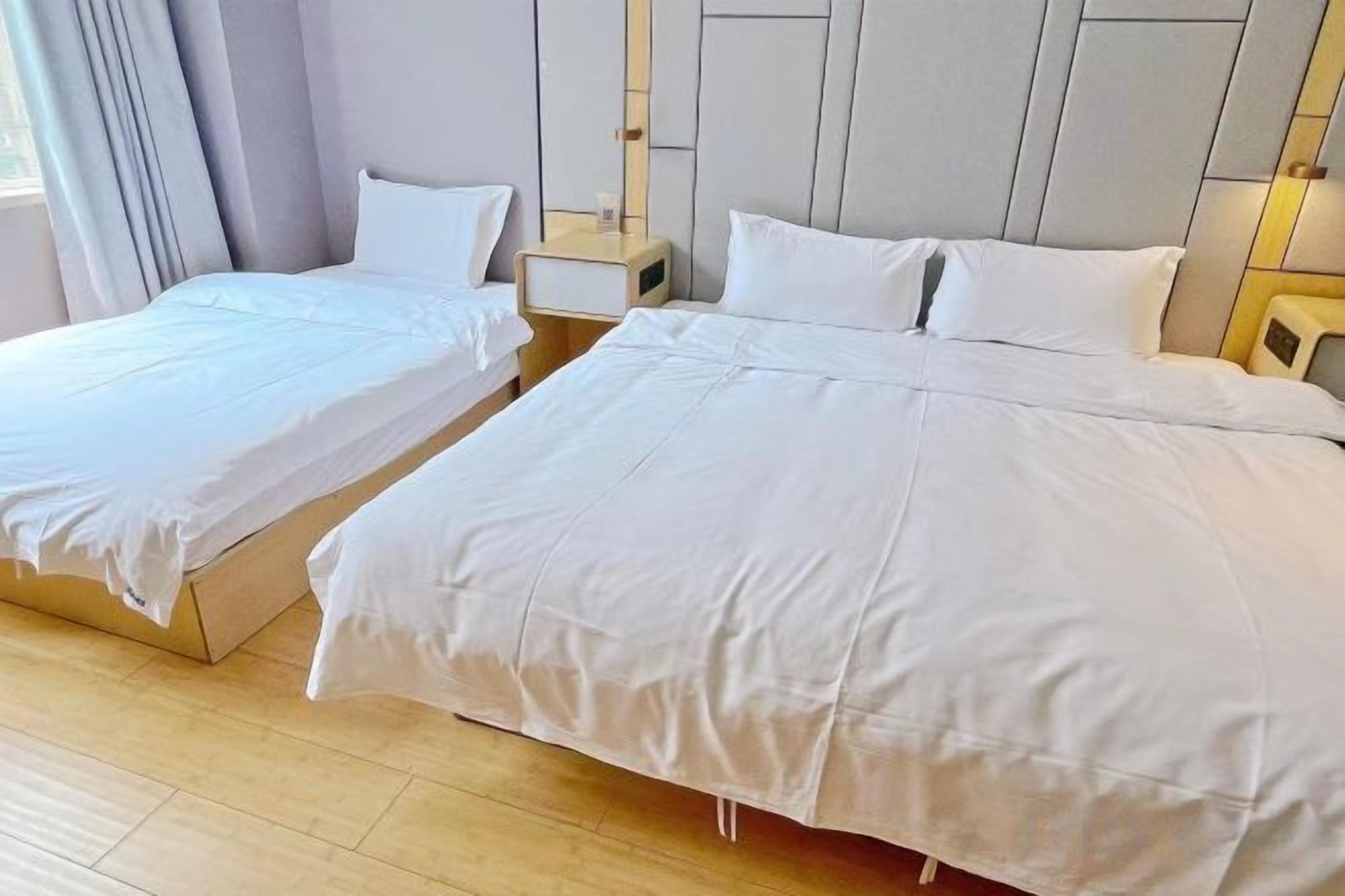 Habitación de hotel con dos camas individuales y una cama más grande, suelo de madera y una decoración en tonos neutros.