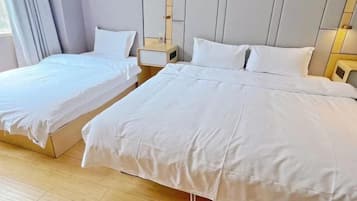 Habitación de hotel con dos camas individuales y una cama más grande, suelo de madera y una decoración en tonos neutros.