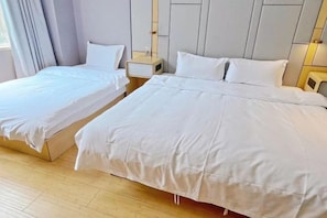 Een hotelkamer met twee enkele bedden en een groter bed, houten vloeren en een neutraal kleurenpalet.