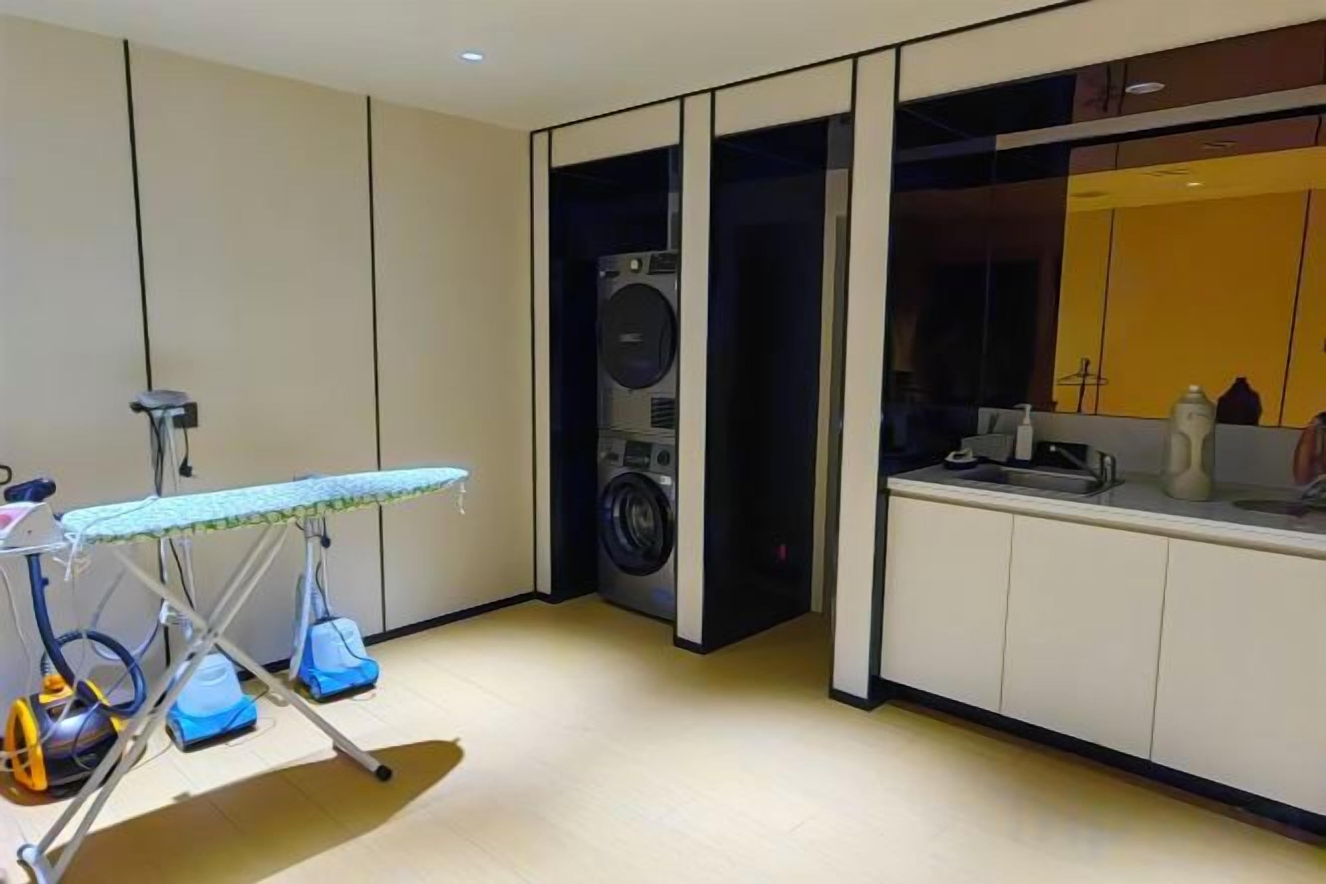 A laundry area with a washing machine, ironing board, and a sink.