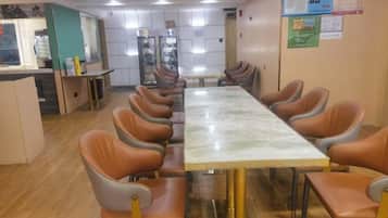 Sala de conferências com uma mesa grande e várias cadeiras, área de kitchenette e um quadro de avisos.