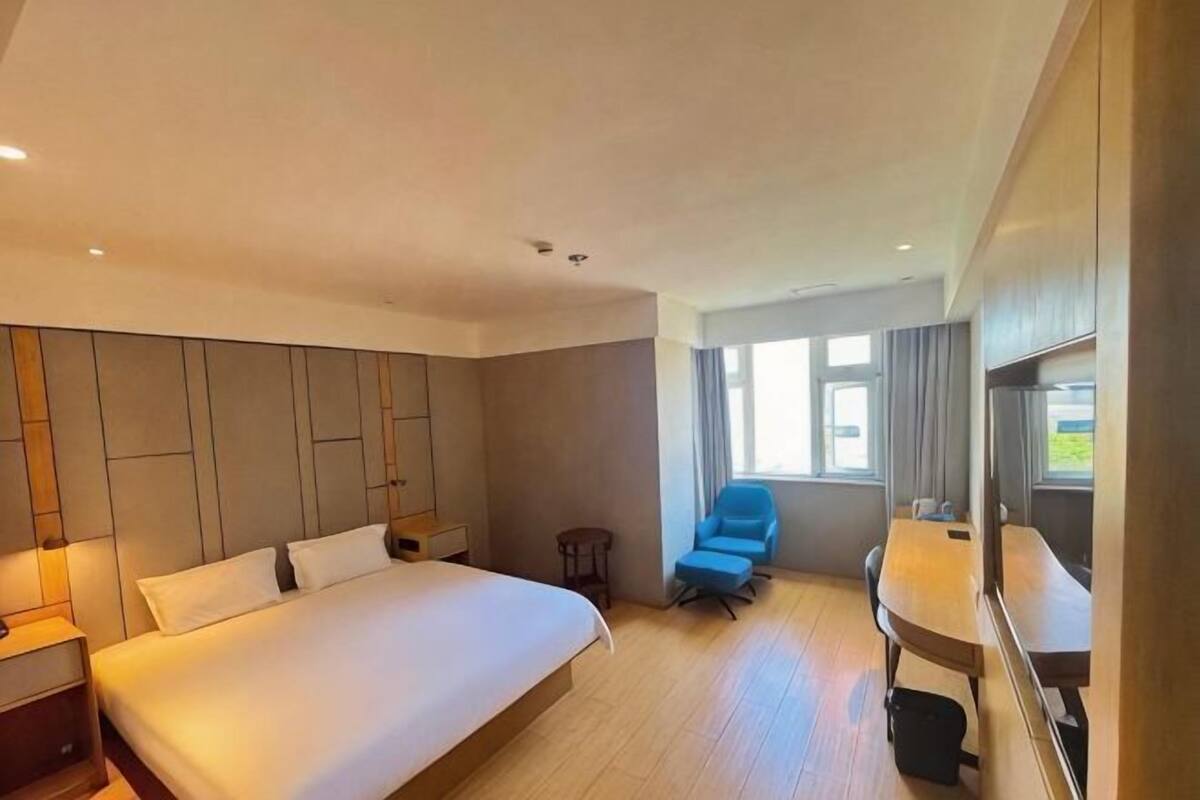 Ein Hotelzimmer mit einem großen Bett, einem Schreibtisch, einem Stuhl und Blick ins Freie.