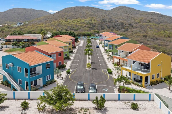 Un barrio residencial con casas coloridas, una calle central y una montaña al fondo.