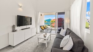 Una sala moderna con un televisor de pantalla plana, consola blanca, sofá gris y puerta de vidrio que da a un área de estar exterior con sillas.