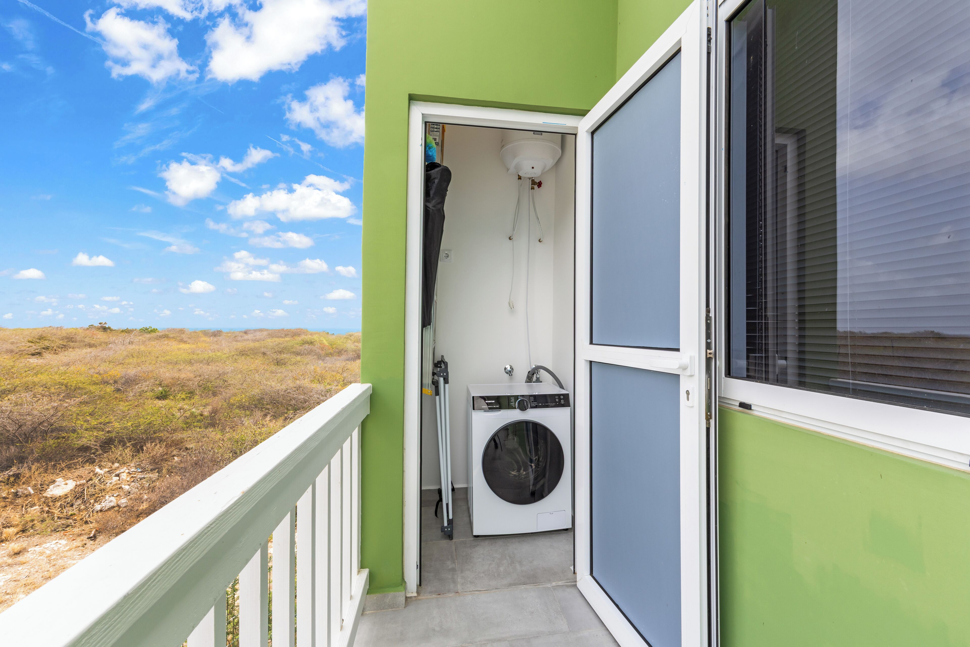 Ein Balkon mit Waschmaschine und Trockner, eine Tür zu einem Waschraum sowie Blick auf den Strand.