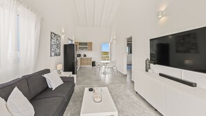 Una sala de estar moderna con un sofá gris, una mesa de centro blanca y un televisor grande sobre un mueble blanco.