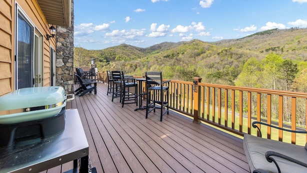 A wooden deck with outdoor seating, a stone wall, and a view of rolling hills. - Newly Renovated Condo in Gated Golf Community (Whittier)
