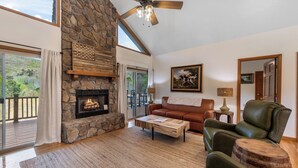 A spacious living room with a stone fireplace, leather furniture, and a balcony with a view of the outdoors. - Newly Renovated Condo in Gated Golf Community (Whittier)