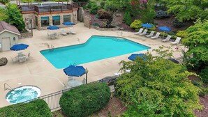 A pool area with lounge chairs and umbrellas, a hot tub, and a stone building with windows. - Newly Renovated Condo in Gated Golf Community (Whittier)