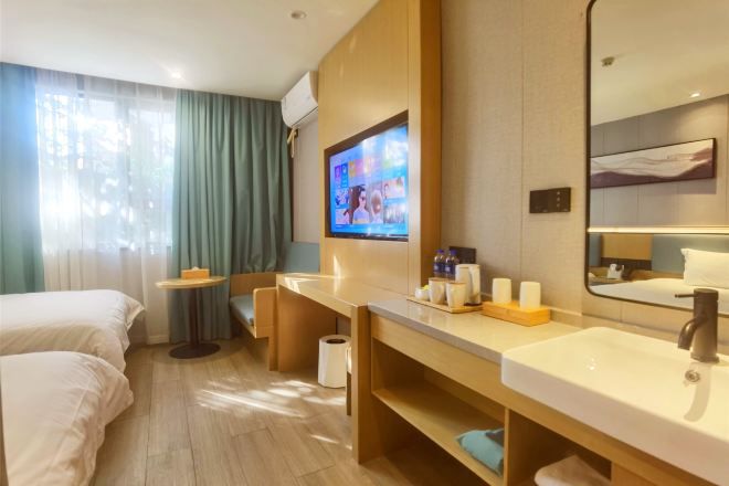 Een hotelkamer met een bed, een bureau, een televisie, een badkamer met een wastafel en spiegel, en een raam met gordijnen.