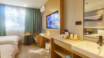 Een hotelkamer met een bed, een bureau, een televisie, een badkamer met een wastafel en spiegel, en een raam met gordijnen.