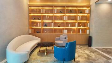 A modern lounge area with a sofa, chairs, and a wooden bookshelf.
