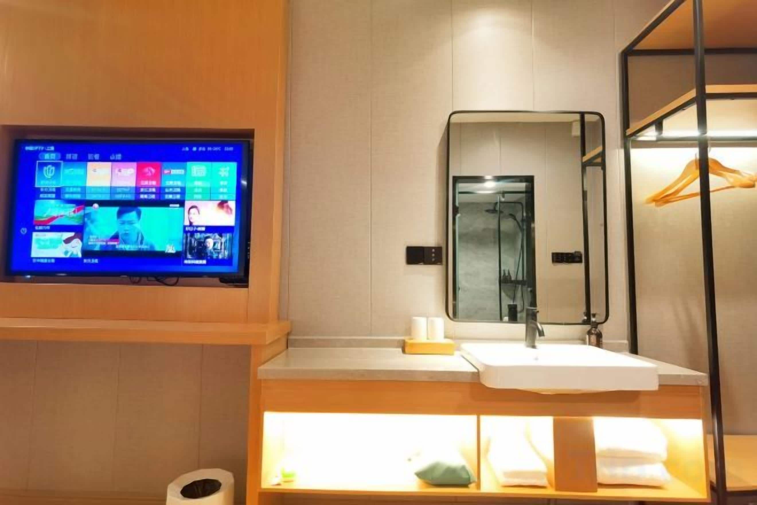 A modern bathroom with a digital screen, a mirror, a sink, and a towel rack.