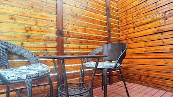 A covered outdoor area with wooden slats, wicker chairs, and a small table.