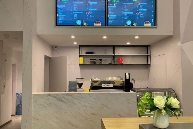 A modern reception area with a marble counter, a coffee machine, and a menu display.