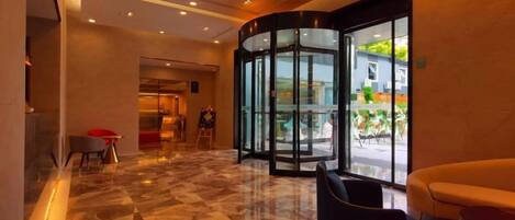 A hotel lobby with a revolving door, a reception desk, and a seating area.