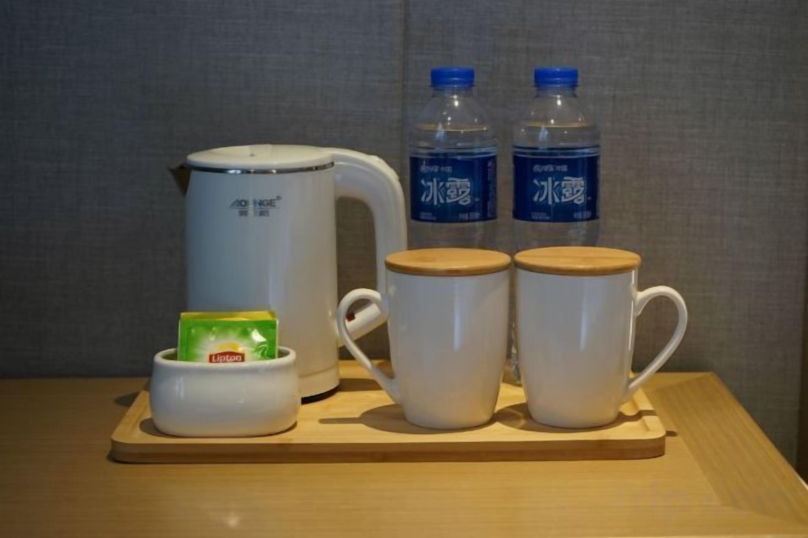Een tafel met een witte elektrische waterkoker, twee waterflessen, twee witte mokken en een klein bakje met een groen zakje.