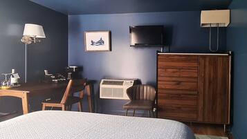 A hotel room with a bed, a desk with a lamp, a chair, a television, an air conditioner, and a wardrobe.