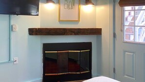 Una habitación con una cama, un televisor montado, un cuadro enmarcado y una ventana con vista a edificios.