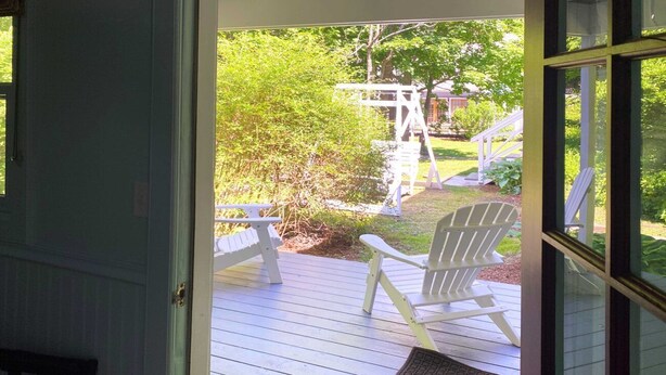 Una terraza de madera con sillas Adirondack y una pequeña mesa, que da a un jardín con un columpio.