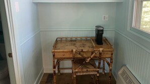 Una habitación pequeña con una mesa de bambú, un calentador y un estante con mantas dobladas.