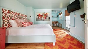 Un dormitorio con cama, televisión y una zona de cocina al fondo.