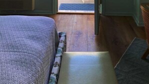 Ett sovrum med en säng, en bänk, en dörr som leder ut till en uteplats och en väggmonterad ventilationsöppning.