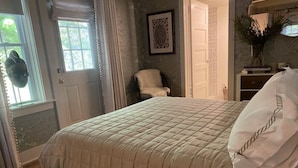 Ein Schlafzimmer mit einem großen Bett, einem Sessel, einer Tür und einem Fenster mit Vorhängen.