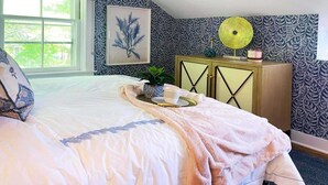 Une chambre à coucher avec un lit, une table de chevet avec une lampe, une fenêtre et un papier peint à motifs.
